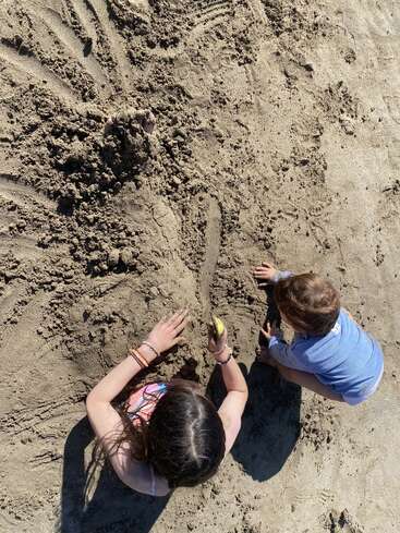 Dos niños juegan juntos en una playa de arena, cavando y dibujando en la arena bajo el sol radiante, creando formas divertidas y disfrutando de un despreocupado día de verano.