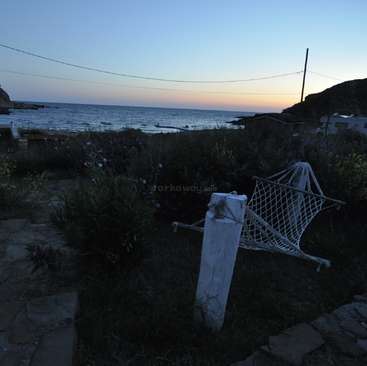 The image depicts a serene coastal scene at dusk, featuring a white net, a wooden post, and a stone pathway, set against a tranquil ocean backdrop.