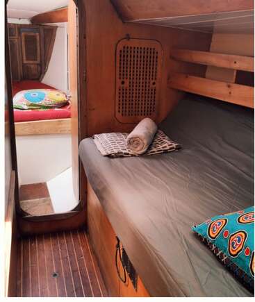 This cozy cabin interior features two beds with colorful pillows, wooden walls and floors, linens neatly folded, and ample natural light, creating a warm and inviting atmosphere.