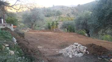 La imagen representa un patio con una gran superficie abierta, con un parche de tierra y una pequeña colina, rodeado de árboles y arbustos, con algunos objetos dispersos.