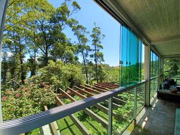This image shows a sunlit room with large glass windows overlooking a lush, green garden and tall trees, creating a peaceful, nature-filled, and inviting environment.