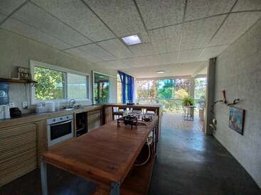 This image shows a modern, open kitchen with a wooden island, stove, oven, large windows, plants, and views of greenery outside, creating a bright atmosphere.