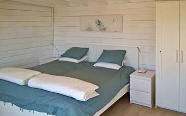 Cette chambre confortable comprend un grand lit avec des draps sarcelle, deux oreillers, des couettes blanches, deux tables de chevet avec lampes, une armoire et une peinture murale minimaliste.