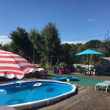 A imagem mostra uma cena de piscina no quintal com um guarda-sol listrado vermelho e branco, piscina azul e mobília de pátio, em um cenário sereno de árvores e um céu azul claro.