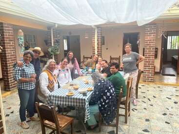 A group of twelve people gather around a table covered with a checkered cloth, enjoying a meal and each other's company in a cozy courtyard setting.