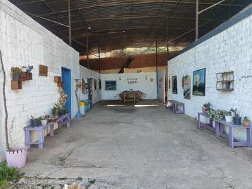 This image shows an open, roofed courtyard with white brick walls, decorated with potted plants, artwork, benches, and a table set at the far end.