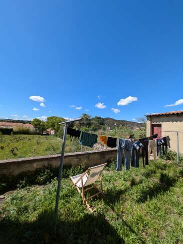 A sunny backyard scene with clothes drying on a line, a chair on green grass, blue sky above, and mountains in the background, creating a peaceful atmosphere.