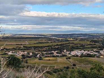 This image shows a picturesque rural landscape with patchwork fields, clusters of houses, distant hills, and a sky covered by a blanket of dramatic clouds.