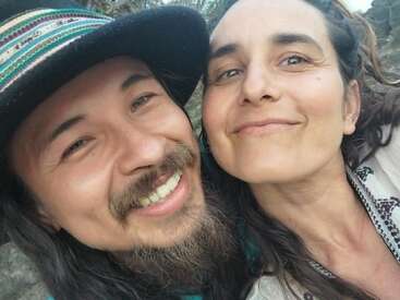 Ein lächelnder Mann und eine lächelnde Frau machen draußen ein Selfie aus nächster Nähe. Er trägt einen bunten Hut und hat einen Bart. Sie sehen glücklich aus und genießen die gemeinsame Zeit.