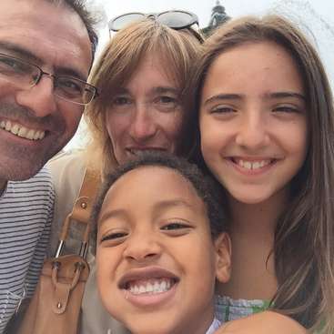 L'image représente une famille de quatre personnes posant pour un selfie : un homme, une femme et deux enfants, tous souriants et regardant l'appareil photo.