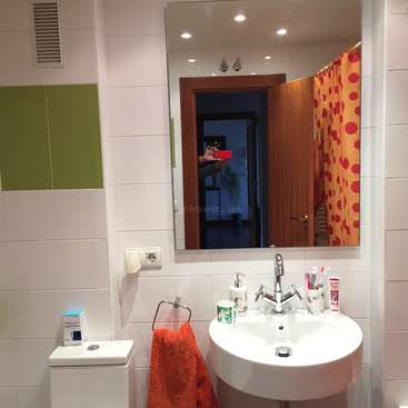 L'image représente une salle de bains avec un lavabo, un miroir et des toilettes blancs, avec une serviette rouge suspendue au lavabo et un rideau de douche à pois rouges.