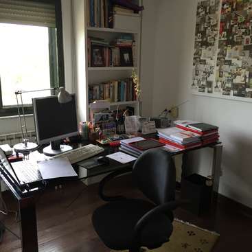 L'image représente un bureau encombré composé d'un bureau, d'une chaise, d'un ordinateur et d'une étagère, avec une fenêtre et un collage sur le mur.