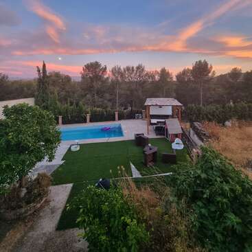 The image depicts a serene backyard with a pool, gazebo, and lush greenery, set against a picturesque sunset sky with pink clouds.