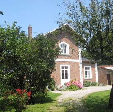 L'image représente une charmante maison en briques à deux étages avec des bordures blanches, nichée au milieu d'arbres luxuriants et de fleurs éclatantes par une journée ensoleillée.