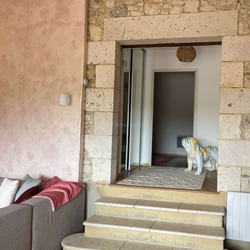 Das Bild zeigt einen gemütlichen Wohnraum mit beigen Steinwänden, einem Sofa mit roten und weißen Kissen, Stufen und einer dekorativen weißen Bulldoggenstatue in der Nähe einer Tür.