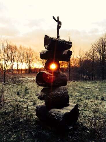 A stack of large, snow-dusted logs stands upright in a field. The sun shines perfectly through a hole in the middle during a golden sunrise.