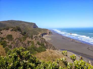 La imagen representa un sereno paisaje costero con un escarpado acantilado, una playa de arena y un vasto océano, sobre un cielo azul despejado.