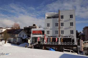 The image depicts a snowy scene with a building in the background, featuring a road and a body of water, likely taken during the day in a rural area.