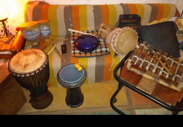 This cozy room features various percussion instruments, including drums, a xylophone, and maracas, all placed on and around a colorful striped sofa and small tables.
