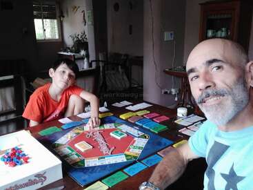 A man and a child play a board game together at a table, smiling and relaxed in a cozy, softly lit room with homey decor.