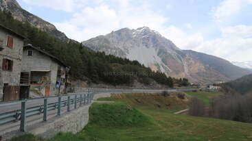 The image depicts a serene mountainous landscape with a road, featuring a mix of greenery and buildings, evoking a sense of tranquility and natural beauty. The scene is characterized by its peaceful ambiance.