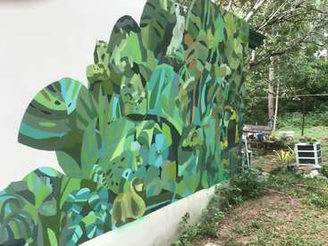 Une peinture murale vibrante de feuilles tropicales verdoyantes recouvre un mur extérieur, se fondant parfaitement dans le jardin environnant et créant une atmosphère artistique et naturelle dans la cour.