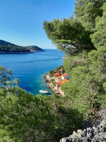 Kristallblaues Wasser trifft auf eine abgelegene Bucht, umrahmt von üppig grünen Kiefern. Zwei kleine Häuser mit roten Dächern überblicken ein ruhiges Boot, das in der Nähe schwimmt.