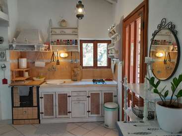 Diese gemütliche Küche hat rustikale weiße Schränke, einen kleinen Herd, hölzerne Akzente, Gewürzregale, einen runden Spiegel, eine Topfpflanze und natürliches Licht durch ein Fenster.