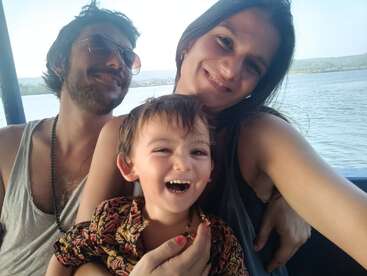 La imagen muestra a una familia de tres miembros posando para un selfie en un barco, con una serena masa de agua y una costa lejana como telón de fondo.