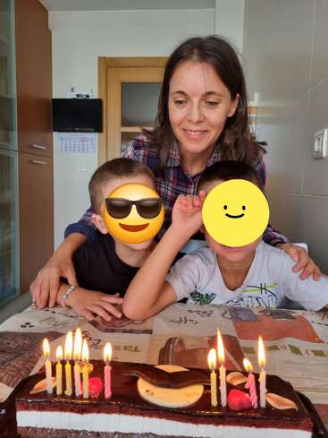 Une femme et deux enfants célèbrent un anniversaire. Les visages des enfants sont recouverts d'autocollants emoji. Un gâteau au chocolat avec des bougies allumées se trouve devant eux.
