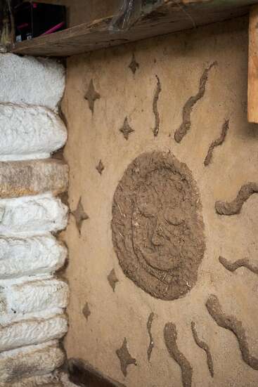 Esta imagen muestra una pared rústica en la que se aprecia un sol con una cara sonriente, estrellas y rayos, todo ello esculpido en arcilla. La estructura que la rodea está formada por bolsas blancas.