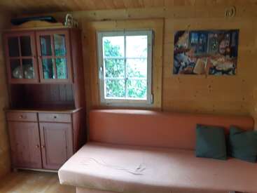 Dieses gemütliche Zimmer aus Holz hat ein Fenster, ein rotes Sofa mit zwei Kissen, einen Holzschrank und ein gerahmtes Bild an der Wand über dem Sofa.