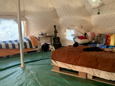 Dieses gemütliche Zelt ist mit zwei Palettenbetten, einer Gitarre, einem kleinen Tisch, Kissen, Decken und Campingutensilien ausgestattet und schafft so einen komfortablen und einladenden Glampingplatz.