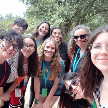 L'image montre un groupe de neuf jeunes posant pour un selfie devant des arbres, la plupart portant des cordons et certains ayant de la peinture noire sur le visage.