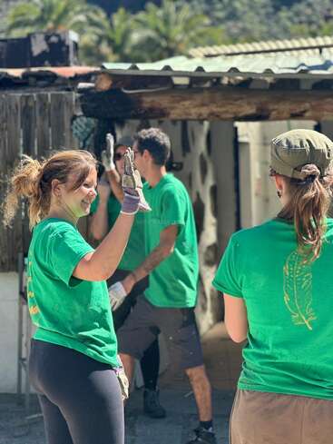 Eine Gruppe von Leuten in grünen T-Shirts steht draußen, lächelt und klatscht sich ab – das vermittelt den Eindruck von Teamwork bei einem Freiwilligen- oder Gemeinschaftsprojekt bei sonnigem Wetter.