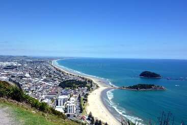 L'image représente une ville côtière avec une plage et une étendue d'eau, avec une route et quelques bâtiments, dans un environnement pittoresque et paisible. L'image a probablement été prise d'un point de vue élevé.