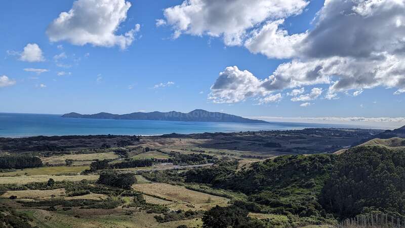 Das Bild zeigt eine ruhige Landschaft mit sanften Hügeln, einem Gewässer und einem klaren Himmel, die ein Gefühl von Frieden und Ruhe hervorrufen. Wahrscheinlich handelt es sich bei der Szene um eine ländliche Gegend oder einen Park.