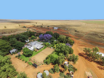 L'image représente un paysage rural avec une grande maison et ses dépendances, entourées d'arbres et d'un chemin de terre, dans un vaste paysage aride.