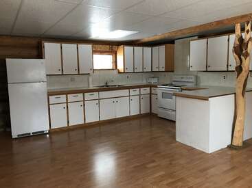 Esta cocina cuenta con armarios blancos, molduras de madera, electrodomésticos blancos, suelo laminado y una singular viga de soporte de madera. Tiene un amplio espacio de almacenamiento y luz natural.