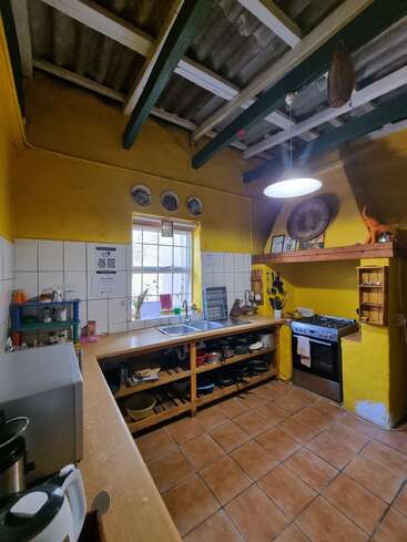 This cozy kitchen features yellow walls, exposed beams, tiled floors, open shelves, a double sink, gas stove, microwave, utensils, and natural light from the window.