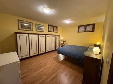 Este dormitorio cuenta con paredes amarillas, suelo de madera, un armario grande, una cama con colcha azul, dos lámparas, una cómoda, un escritorio y cuadros enmarcados.