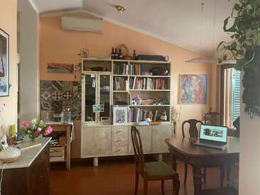 A imagem mostra um cômodo aconchegante com uma estante, uma mesa de jantar e vários itens decorativos, com uma atmosfera calorosa e convidativa.