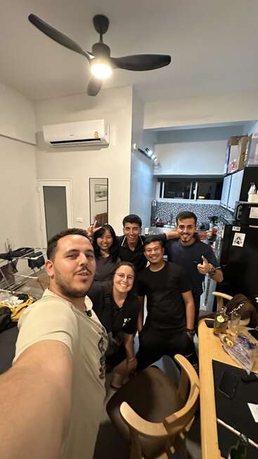 Seis amigos posam alegremente juntos para uma selfie em grupo em uma cozinha moderna e aconchegante. A iluminação quente e os sorrisos genuínos fazem com que o momento seja divertido e memorável.