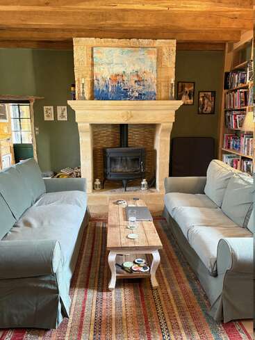 Le salon confortable comprend deux canapés verts, une table basse en bois, des étagères, une cheminée en pierre avec un poêle à bois, des œuvres d'art et un tapis à motifs pour plus de chaleur.