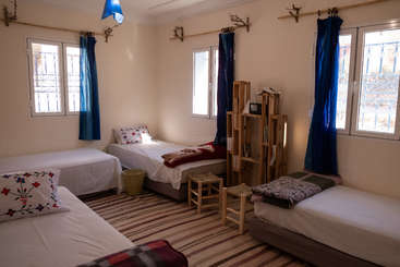 Das Bild zeigt ein Zimmer mit einem Bett, einer Kommode und einem Fenster mit weißem Rahmen und grau-brauner Farbgebung, wobei der Schwerpunkt auf dem Design des Bettes und der umgebenden Möbel liegt.