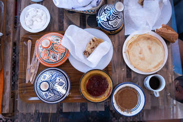 Das Bild zeigt einen Tisch mit verschiedenen Lebensmitteln, darunter Brot, Gemüse und Fleisch, die optisch ansprechend angeordnet sind. Der Tisch ist für eine Mahlzeit gedeckt.