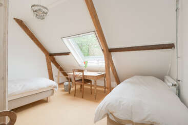 Dieses gemütliche Schlafzimmer im Dachgeschoss verfügt über zwei Einzelbetten, einen Holztisch mit Stühlen, freiliegende Holzbalken, ein Dachfenster, neutrale Farben und einen Kronleuchter.
