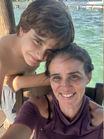 Une femme souriante et un jeune garçon posent côte à côte pour un selfie sur un quai en bois au bord de l'eau, profitant d'une journée ensoleillée et relaxante en plein air.