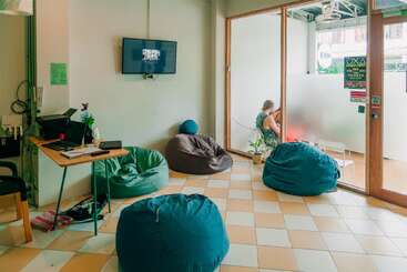 This cozy lounge area features bean bags, a small desk with a computer, a wall-mounted TV, and a glass partition with someone seated outside.