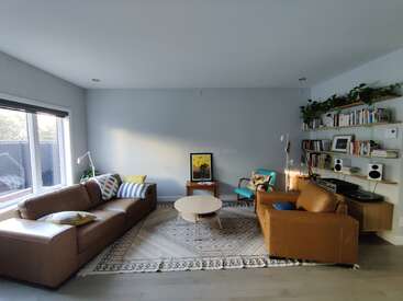 Essa aconchegante sala de estar tem sofás de couro marrom, um tapete estampado, estantes com livros e plantas, uma janela grande, quadros nas paredes e um design moderno e minimalista.
